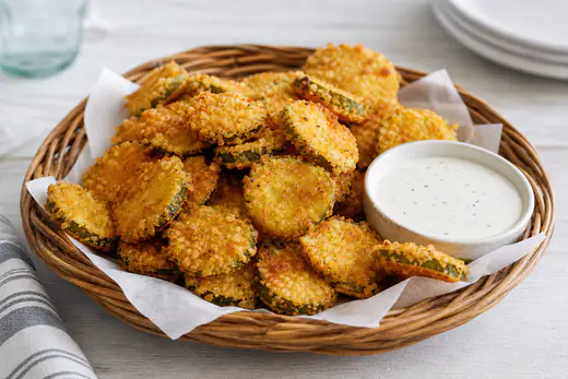 Golden breaded fried pickle chips in a basket with a bowl of ranch dressing