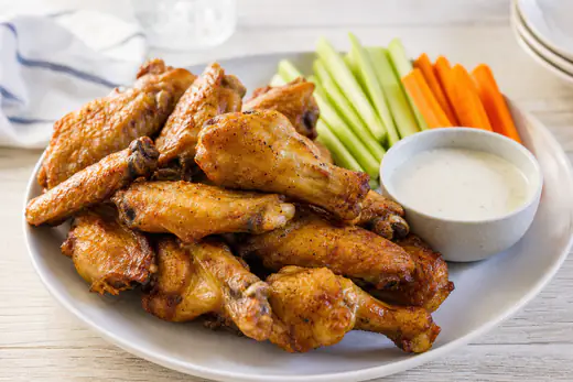 Crispy golden chicken wings piled on a plate with celery sticks and ranch dip