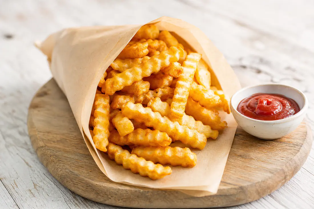 Golden crispy frozen french fries cooked in the air fryer, served in a paper cone with ketchup