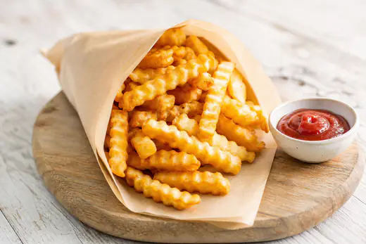 Golden crispy frozen french fries cooked in the air fryer, served in a paper cone with ketchup