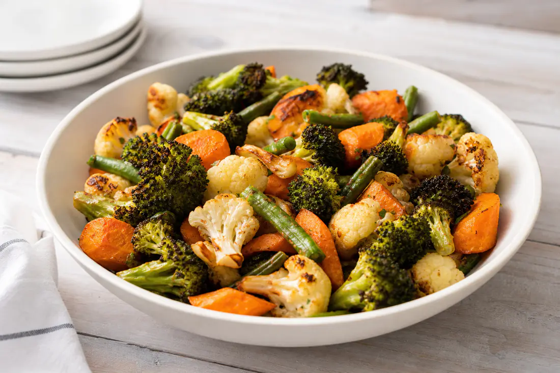 Roasted mixed vegetables with browned edges in a white bowl