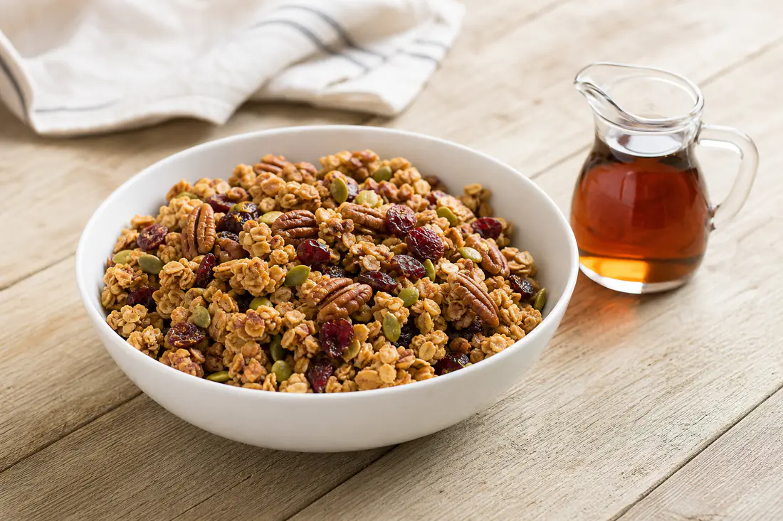 Golden homemade granola clusters with pecans and cranberries in a white bowl