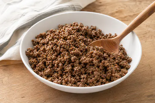 Browned seasoned ground beef crumbles in a white bowl with a wooden spoon
