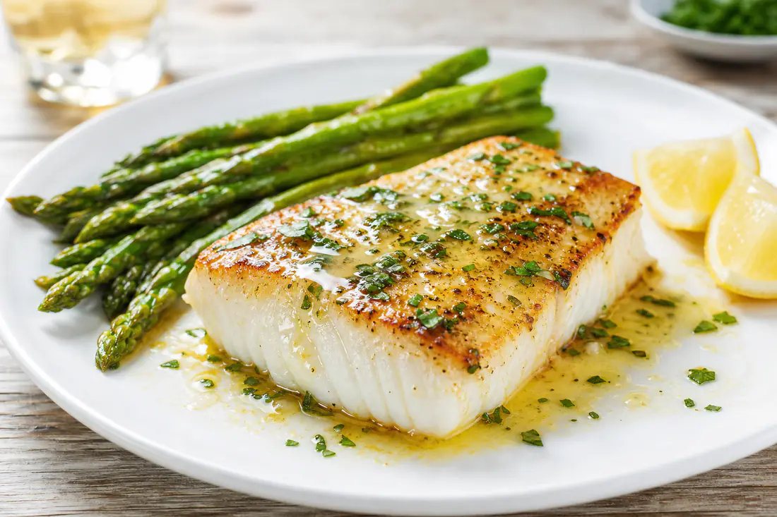 Seared halibut fillet with lemon butter, parsley and a lemon slice on a white plate
