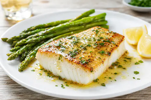 Seared halibut fillet with lemon butter, parsley and a lemon slice on a white plate