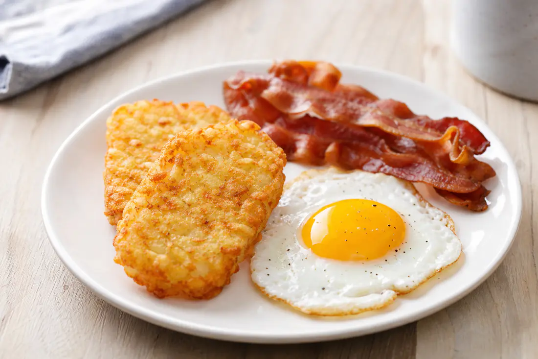Golden crispy hash brown patties on a white plate with fried eggs