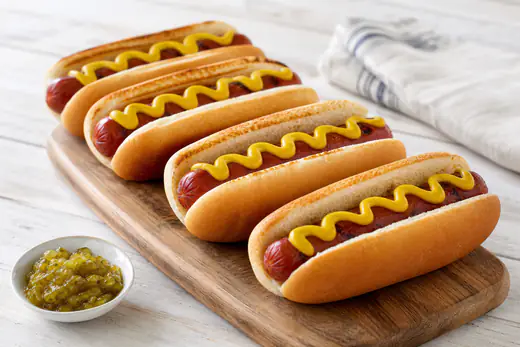 Four air fryer hot dogs in toasted buns topped with mustard on a wooden board