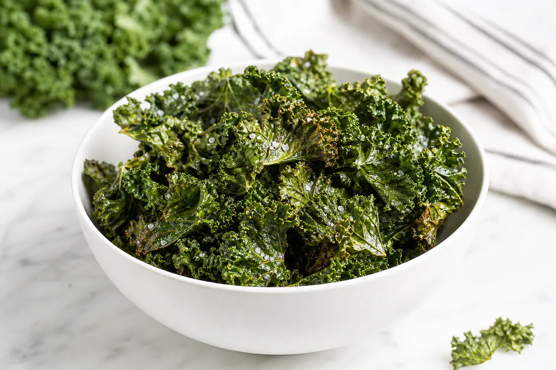 Crispy green kale chips lightly dusted with sea salt in a white bowl