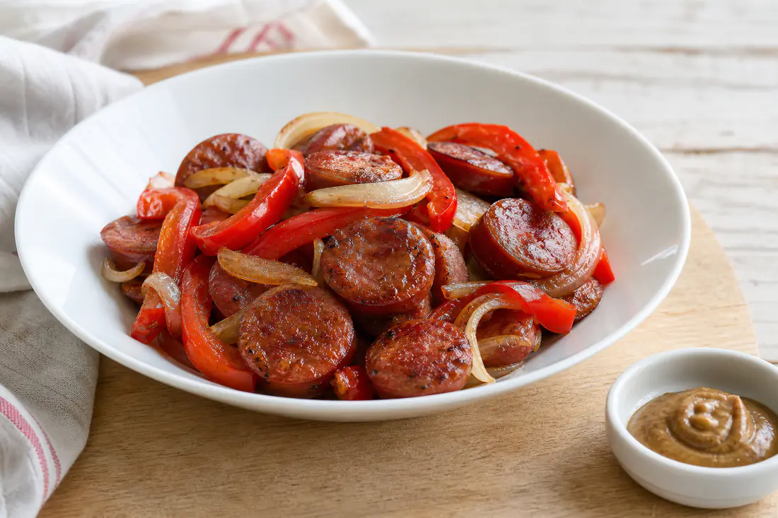 Browned kielbasa slices with bell peppers and onions in a white serving bowl