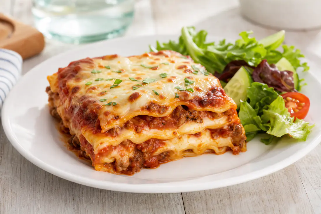A square slice of baked meat lasagna with melted mozzarella and sauce on a white plate