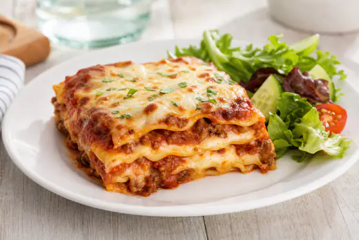A square slice of baked meat lasagna with melted mozzarella and sauce on a white plate