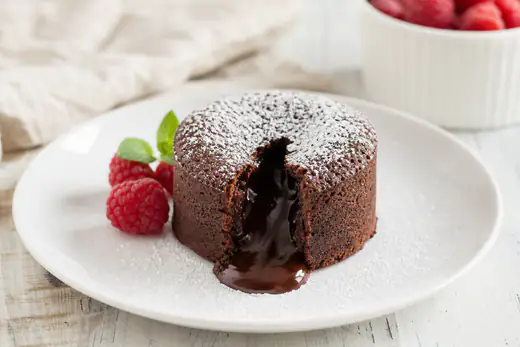 Chocolate lava cake turned out on a plate with molten chocolate flowing from the center and raspberries