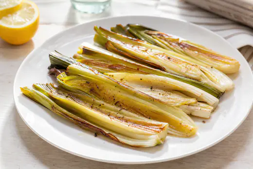 Roasted halved leeks with browned edges drizzled with lemon juice on a white plate