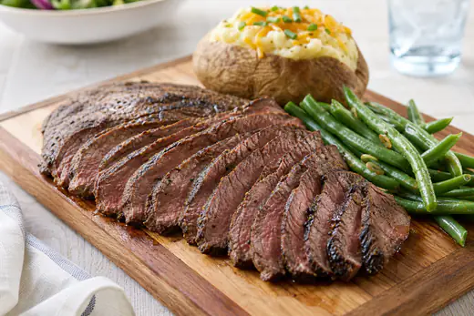 Thin slices of marinated London broil with a browned crust on a cutting board