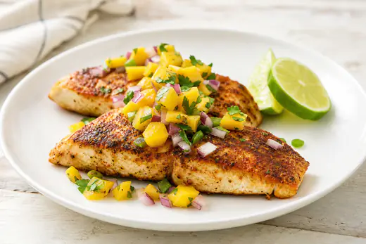 Seasoned mahi mahi fillets with mango salsa and lime wedges on a white plate