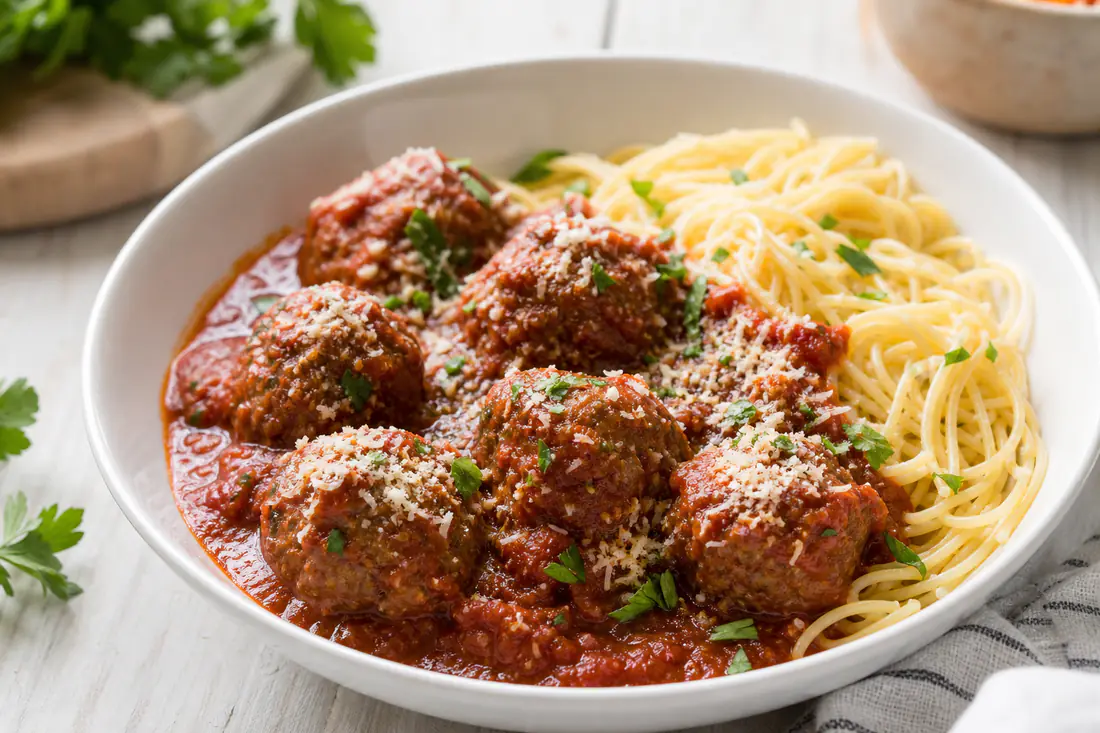 Browned round beef meatballs in a bowl with marinara sauce and fresh parsley