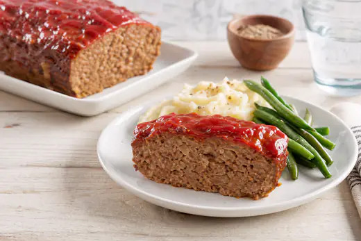 Sliced glazed beef meatloaf with a shiny ketchup topping on a plate with mashed potatoes