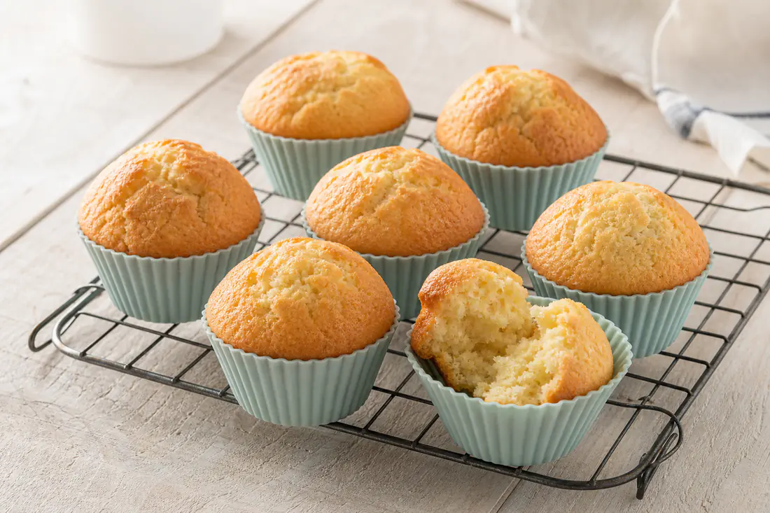 Golden vanilla muffins with domed tops in silicone cups on a wire rack