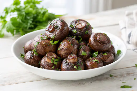 Browned whole cremini mushrooms with parsley in a white bowl