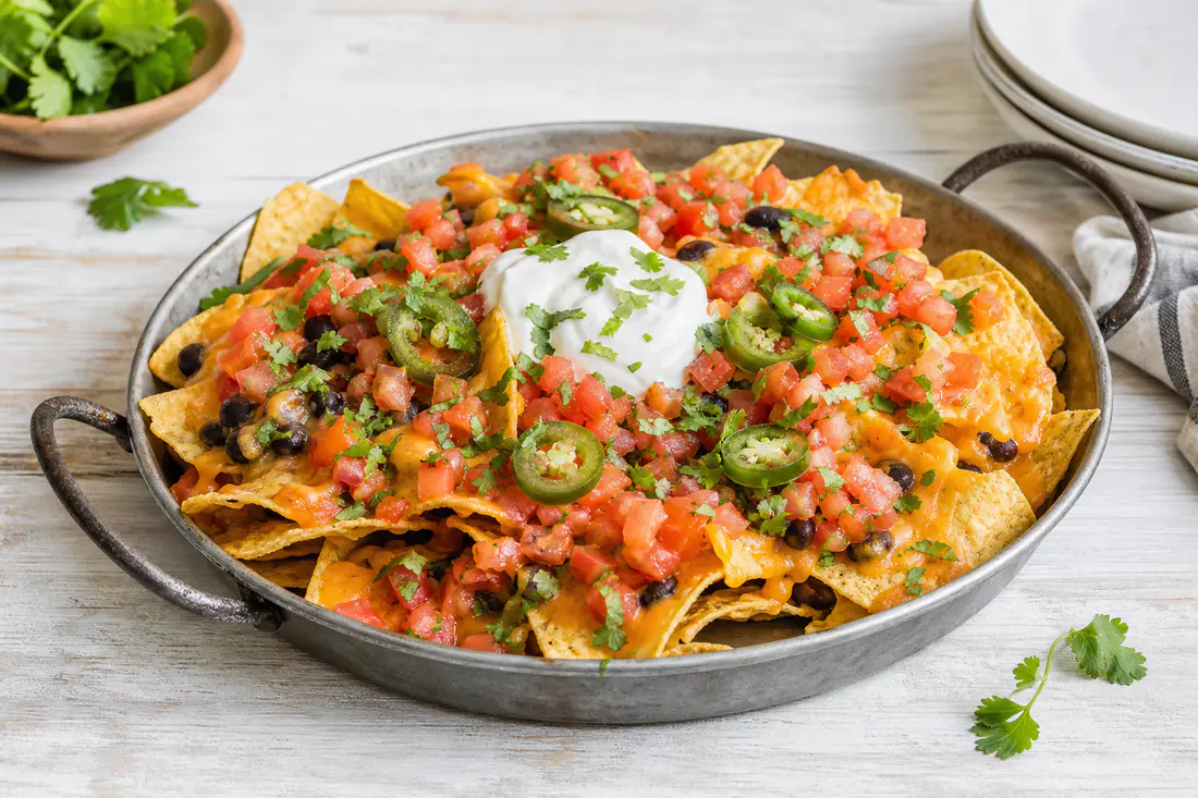 Loaded nachos with melted cheese, black beans, jalapeños, sour cream and cilantro in a small pan