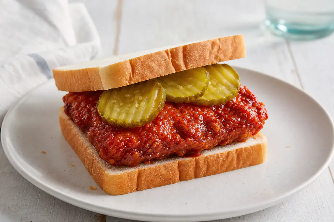 Crispy red-glazed Nashville hot chicken on white bread with dill pickle chips