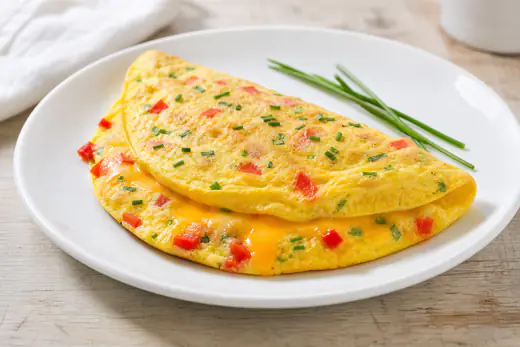 Folded golden cheese omelet with green onions and diced bell pepper on a plate