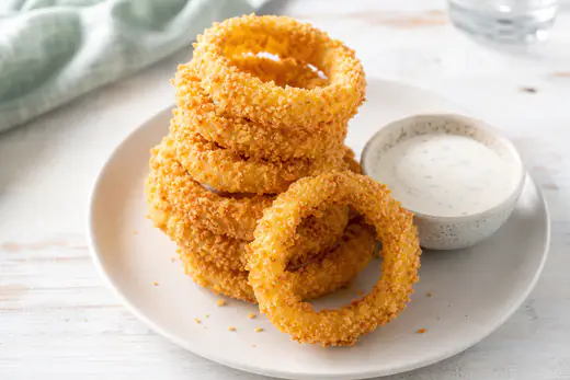 Golden breaded onion rings stacked on a plate with a small bowl of ranch dip
