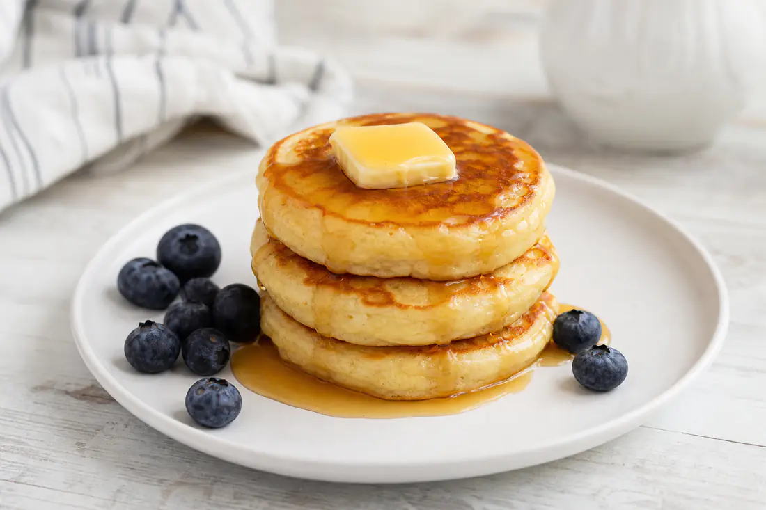 Stack of three fluffy golden pancakes with butter and maple syrup on a plate