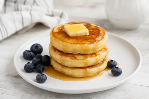 Stack of three fluffy golden pancakes with butter and maple syrup on a plate