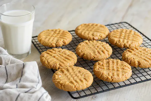 Peanut butter cookies with fork crisscross marks on a wire rack beside a glass of milk