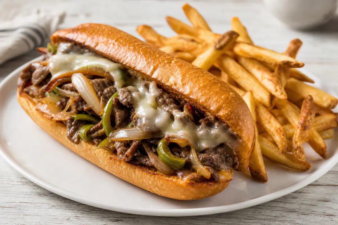 Philly cheesesteak sandwich on a toasted hoagie roll with melted provolone, peppers and onions