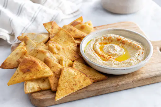 Golden pita chip wedges with a small bowl of hummus and olive oil