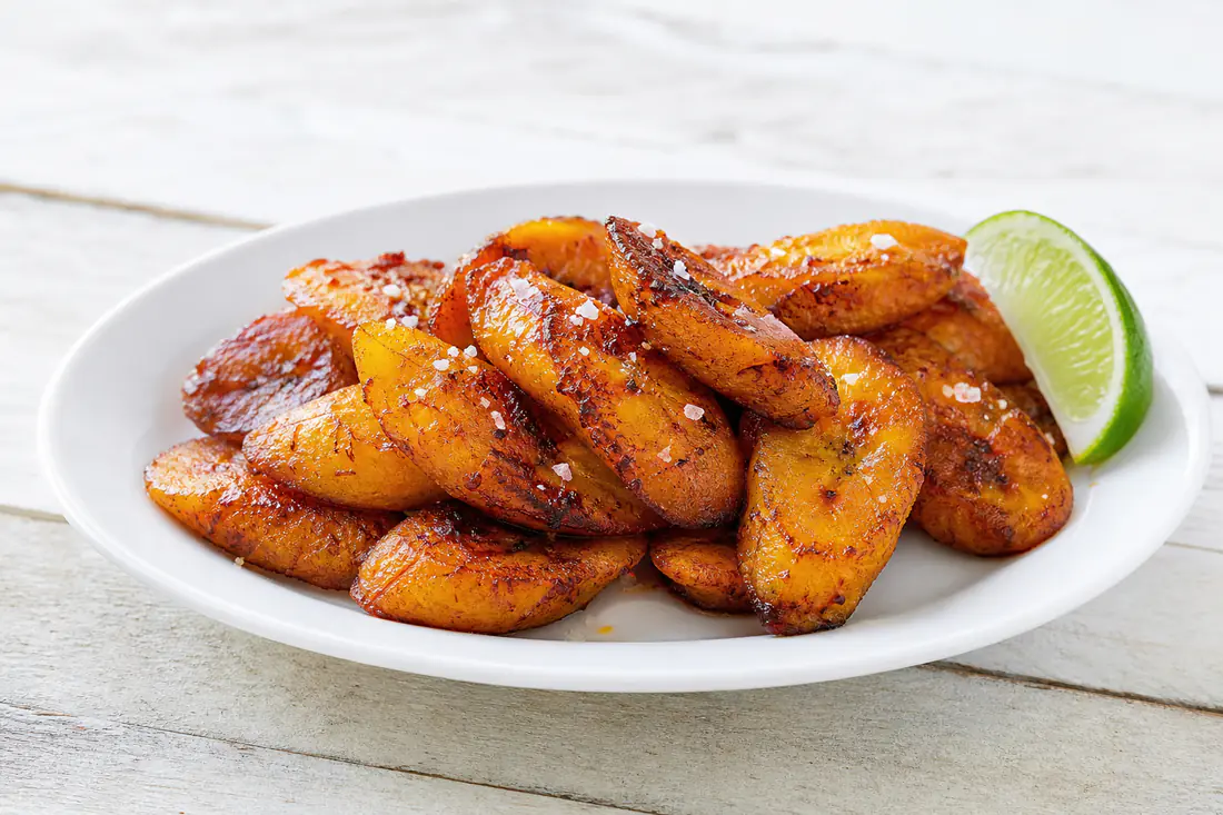 Caramelized golden sweet plantain slices on a white plate with a sprinkle of flaky salt