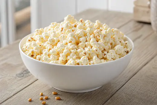 A white bowl of fluffy salted popcorn with a few unpopped kernels at the bottom