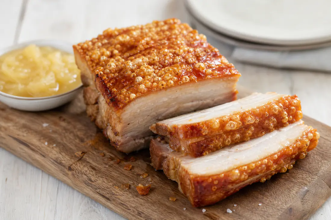 Sliced roasted pork belly with crackling skin on a wooden board