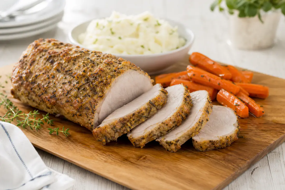 Sliced boneless pork loin roast with a golden herb crust on a cutting board