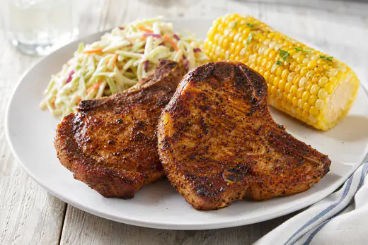 Two browned bone-in pork steaks with a spice rub on a white plate