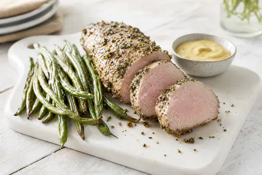 Sliced herb-crusted pork tenderloin with a blush of pink in the center on a white serving board