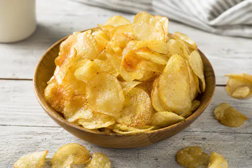 A wooden bowl of thin golden homemade potato chips sprinkled with sea salt