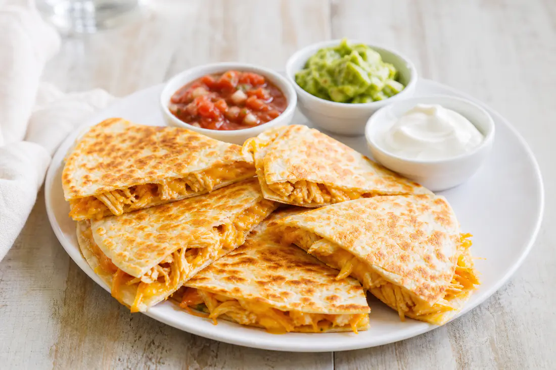 Crisp golden chicken quesadilla cut into wedges with salsa and sour cream on the side