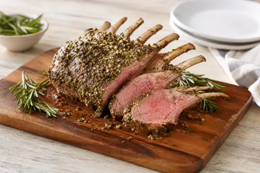 Sliced frenched rack of lamb with a herb crust and a pink center on a board