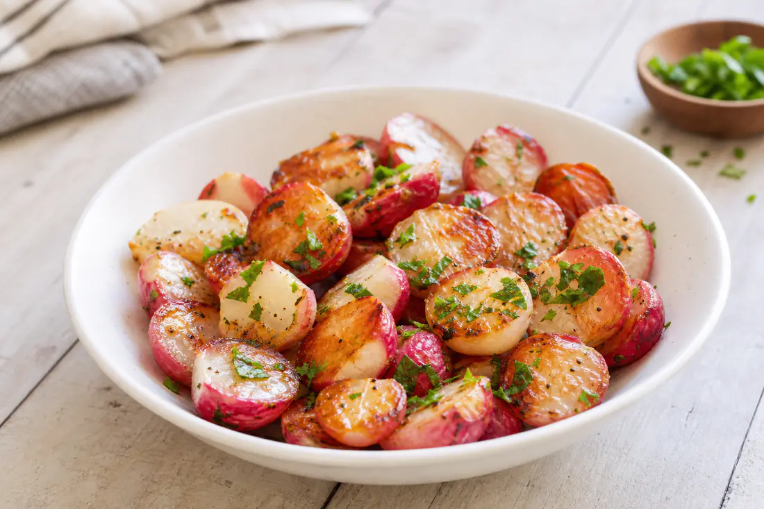 Golden roasted halved radishes with chopped parsley served in a white bowl