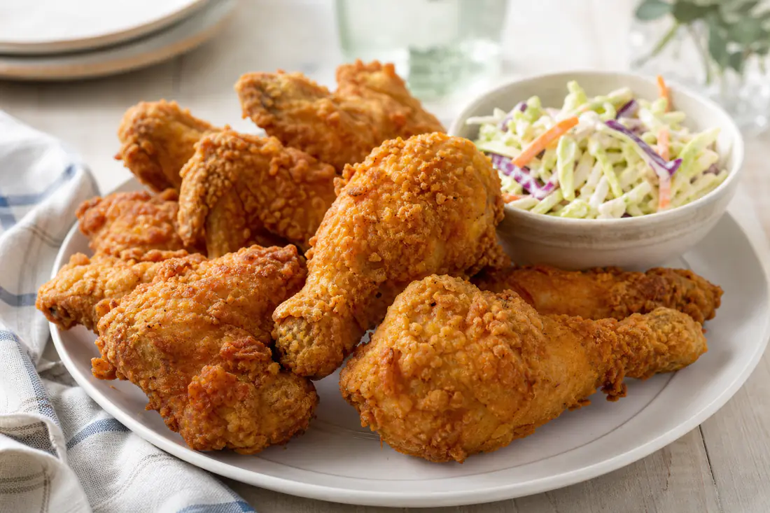Reheated crispy fried chicken pieces and wings on a plate with a side of coleslaw