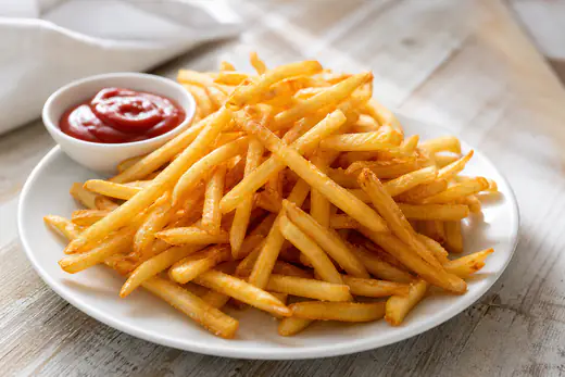 Golden crisp reheated french fries in a pile on a white plate with ketchup