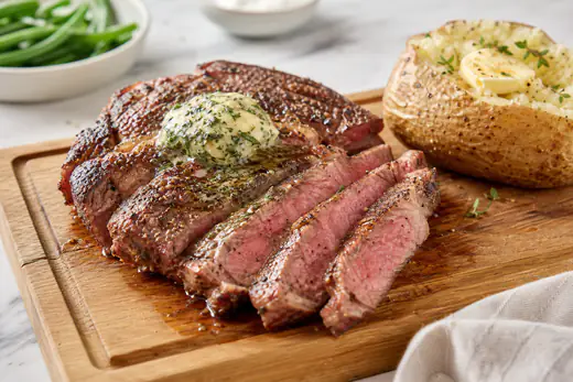 Sliced ribeye steak with a browned crust and herb butter on a cutting board