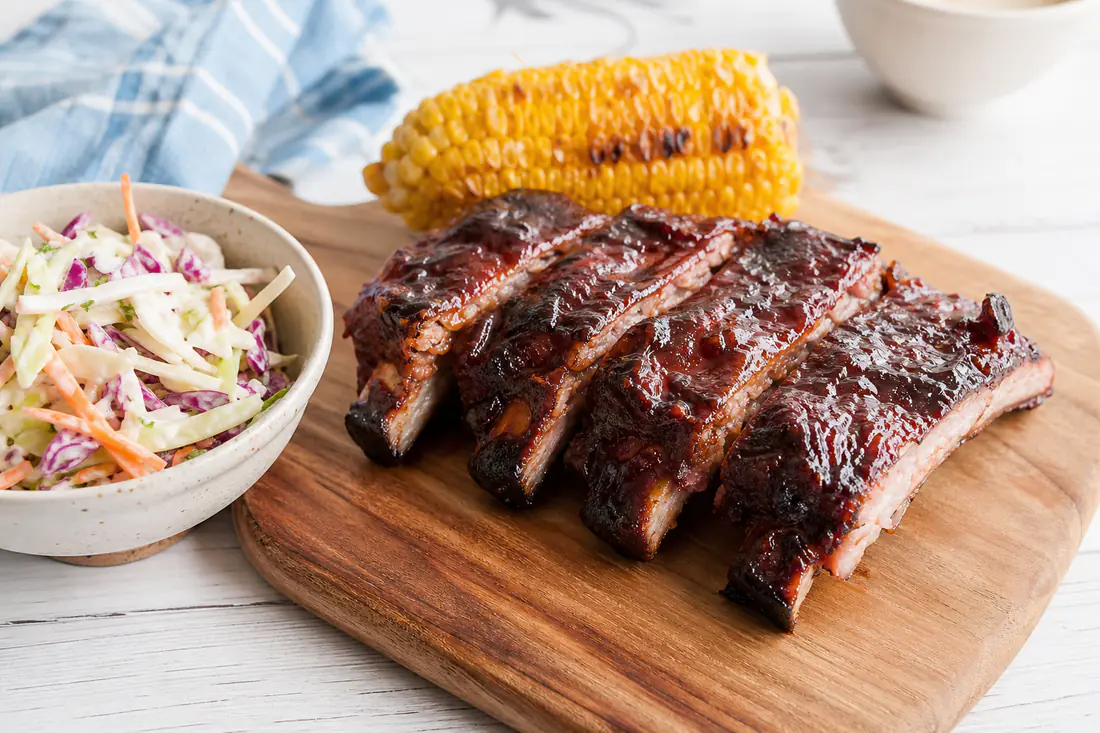 Glazed baby back pork ribs cut into sections on a wooden board