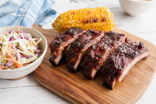 Glazed baby back pork ribs cut into sections on a wooden board