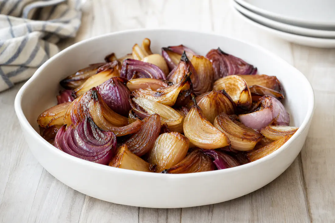 Caramelized red and yellow onion wedges with browned edges in a white serving bowl