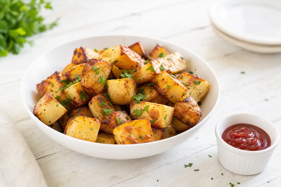 Golden crispy roasted potato cubes with parsley in a white bowl