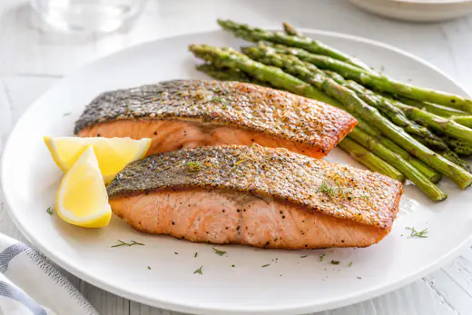 Air fryer salmon fillets with crisp skin and lemon wedges on a white plate with asparagus